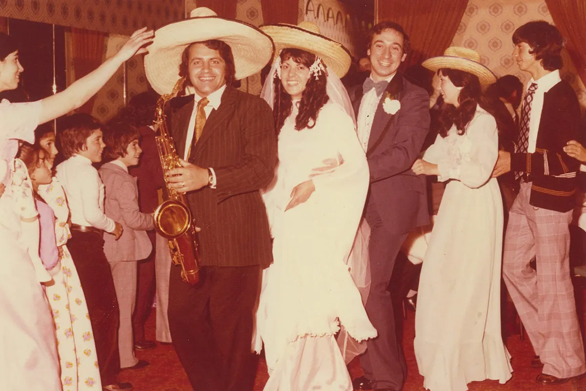 Bride and groom celebrating with guests and a saxophonist, with several people wearing sombreros.