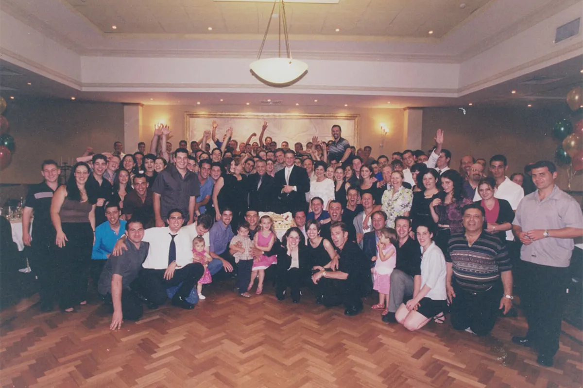 Large group of adults and children posing together on a parquet dance floor in a function room.