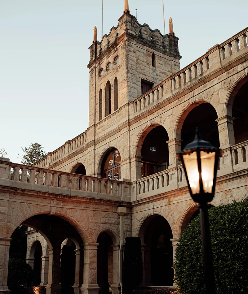 Curzon Hall’s sandstone tower and arched balconies, with a glowing lantern in the foreground