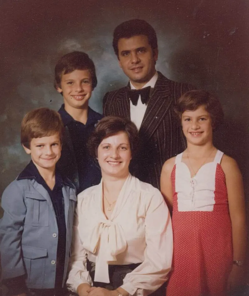 Studio portrait of the Navarra family, with two parents and three children smiling at the camera.