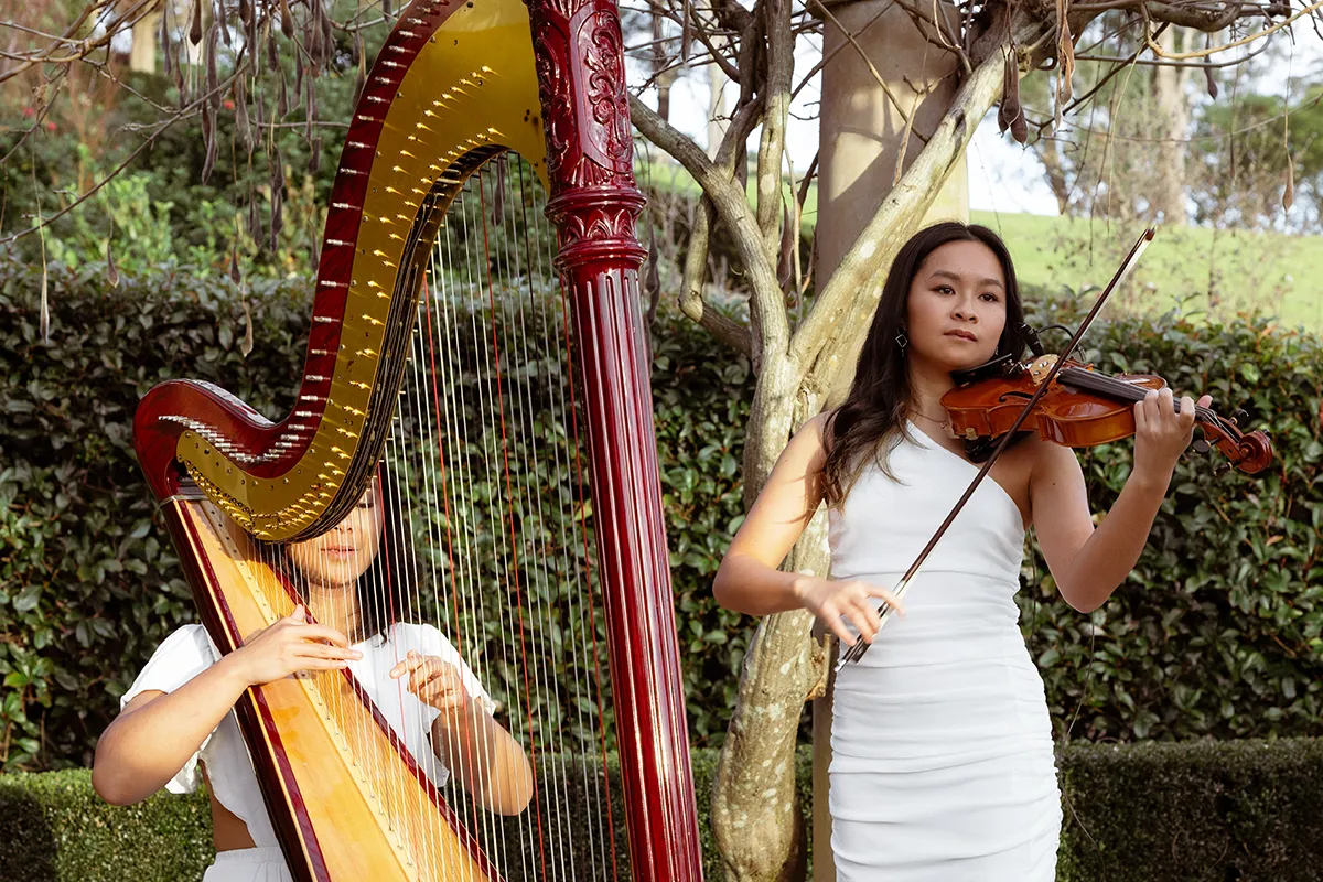 Harpist and violinist performing outdoors as live wedding entertainment